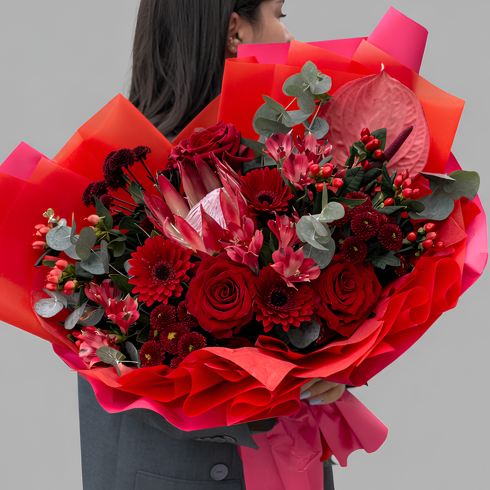 Красный букет из роз, гербер, протеи и антуриума в дизайнерской упаковке